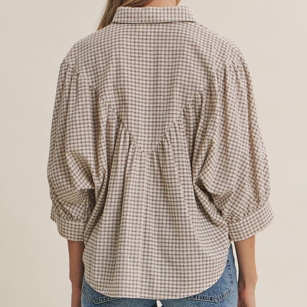 Back view of a woman wearing a plaid, micro-grid button-down shirt with gathered dolman sleeves.