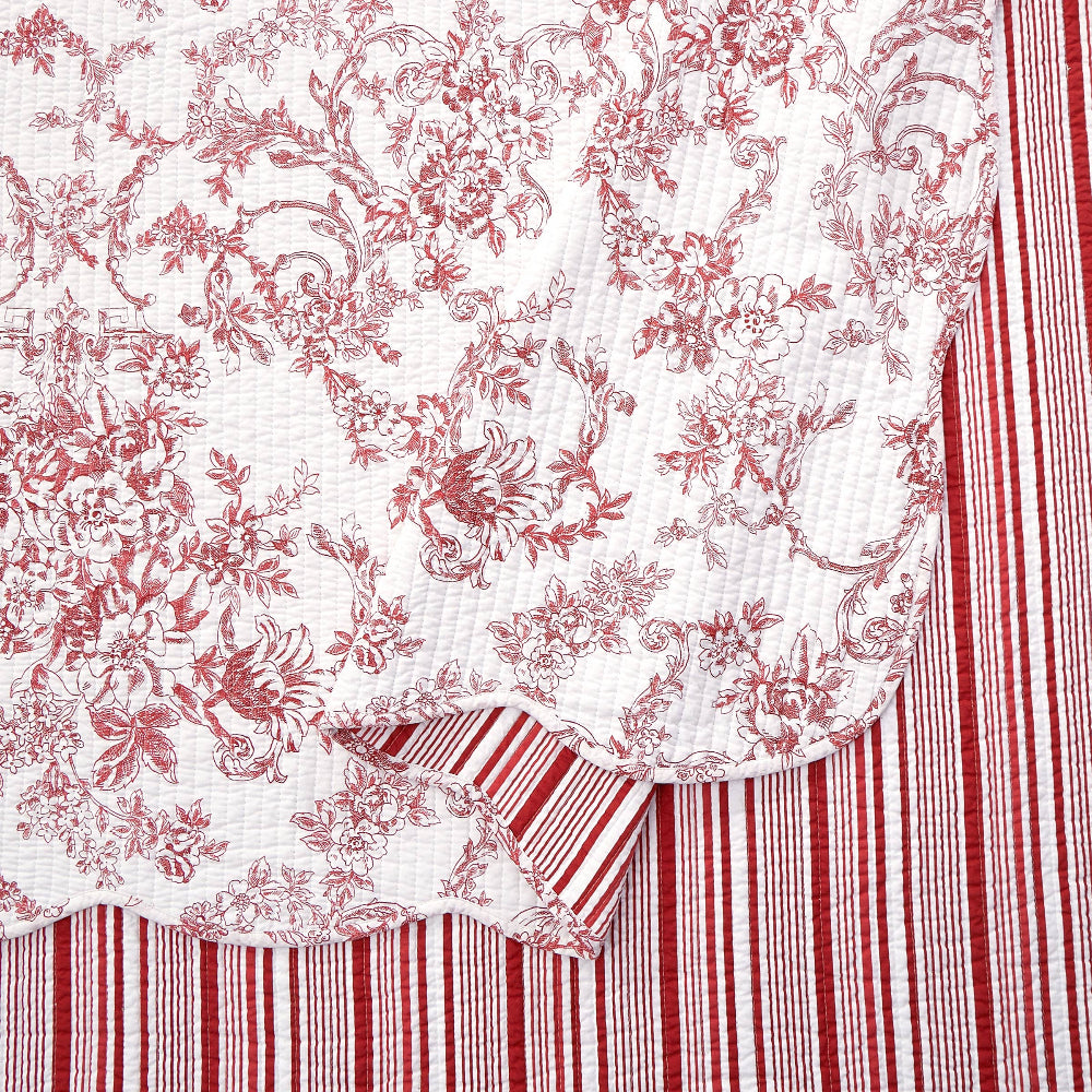 Close-up of red garden toile quilt with scalloped edges and reversible red and white striped pattern.