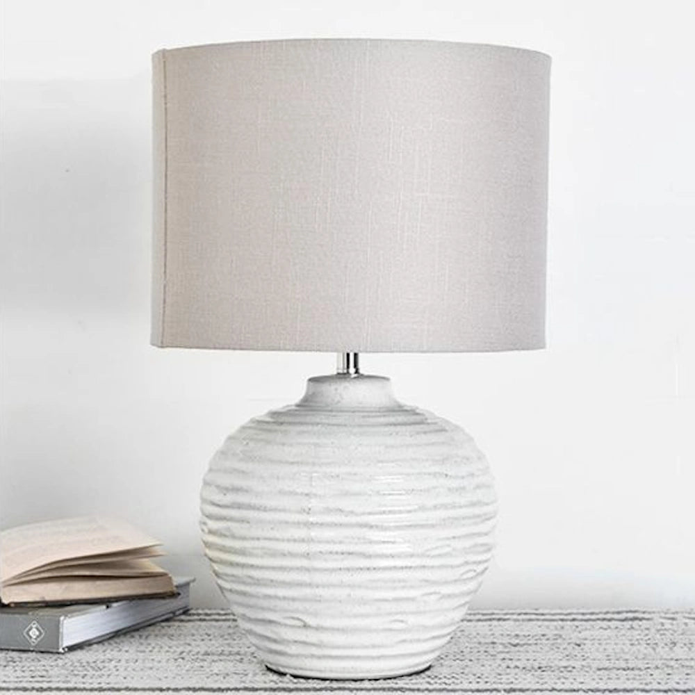 Modern white ribbed ceramic table lamp with a light grey drum shade on a textured surface.