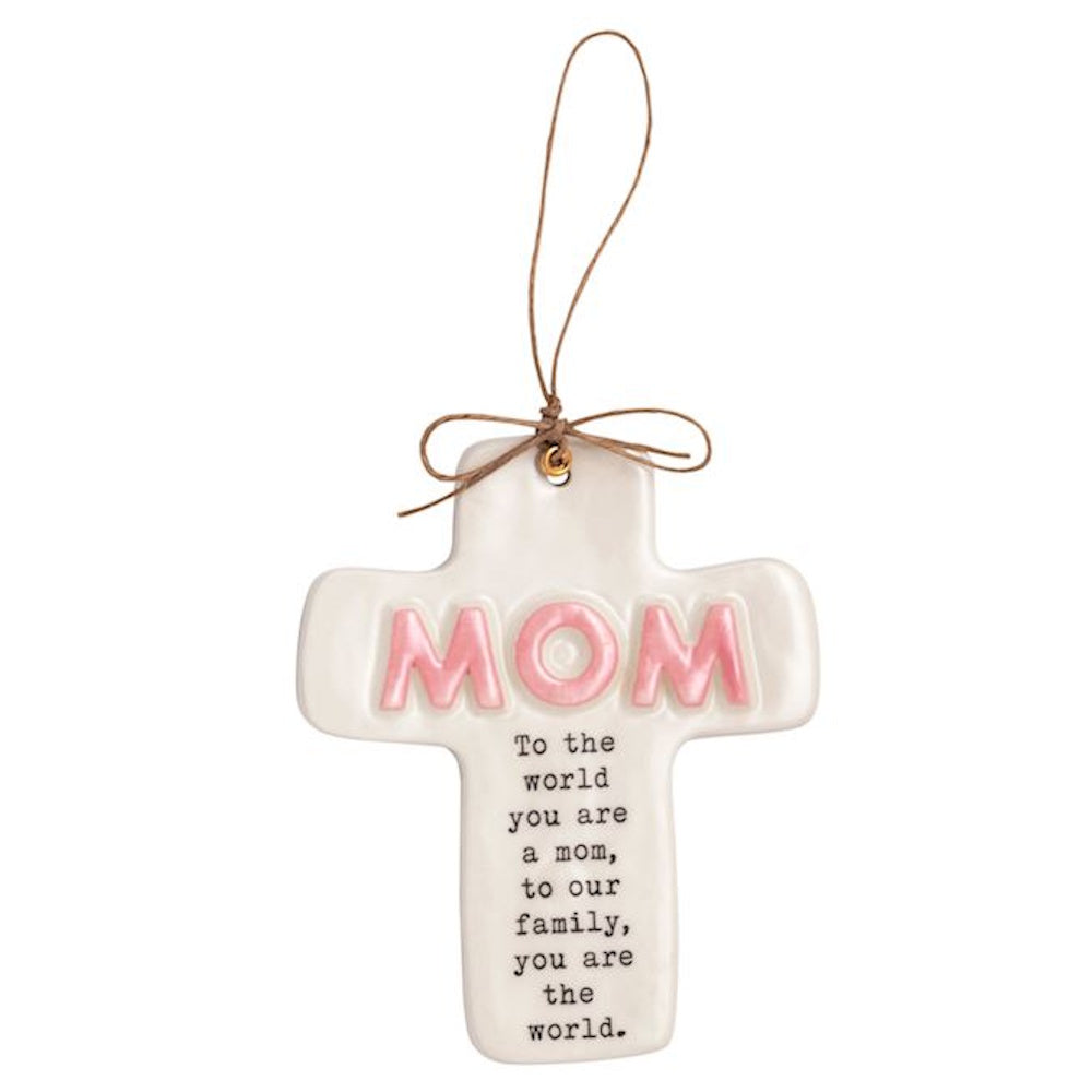 White ceramic cross ornament with pink "MOM" text and a sentimental quote, hanging by a brown twine string.