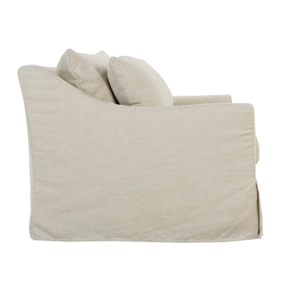 Side profile view of a beige linen slipcovered sofa featuring a sloped arm and loose back cushions.
