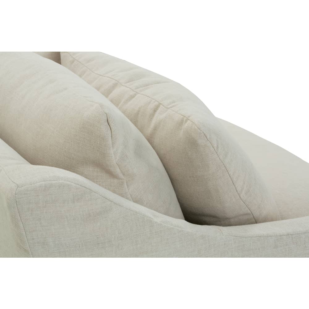 Close-up of plush cushions and a sloped armrest on a beige linen slipcovered sofa.
