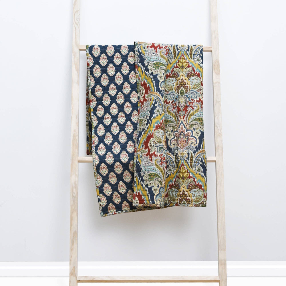 Blue and red bohemian quilted throw with paisley and medallion patterns hanging on a light wood decorative ladder.