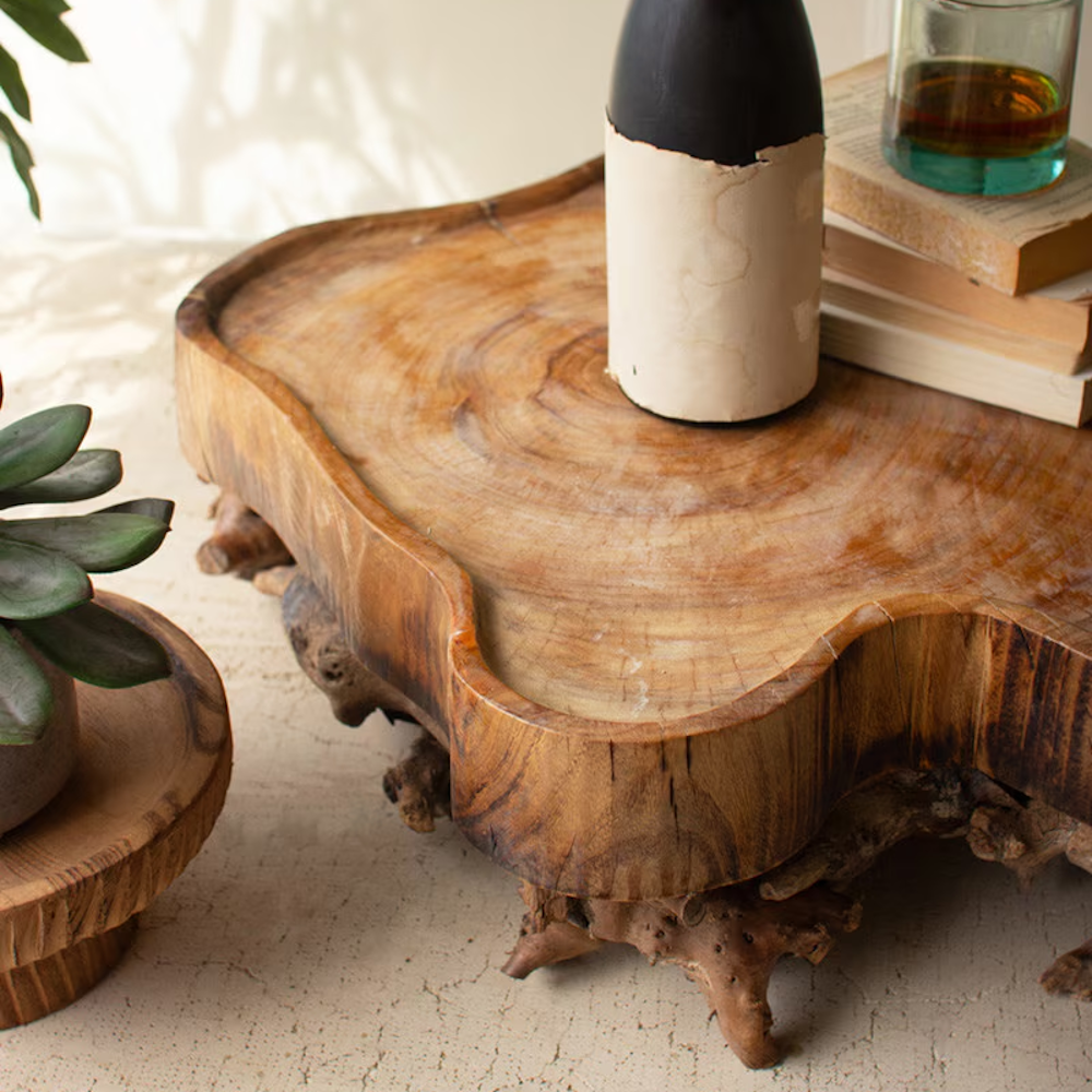 Detailed close-up of a natural wooden slab tray with root legs, holding a bottle and books.