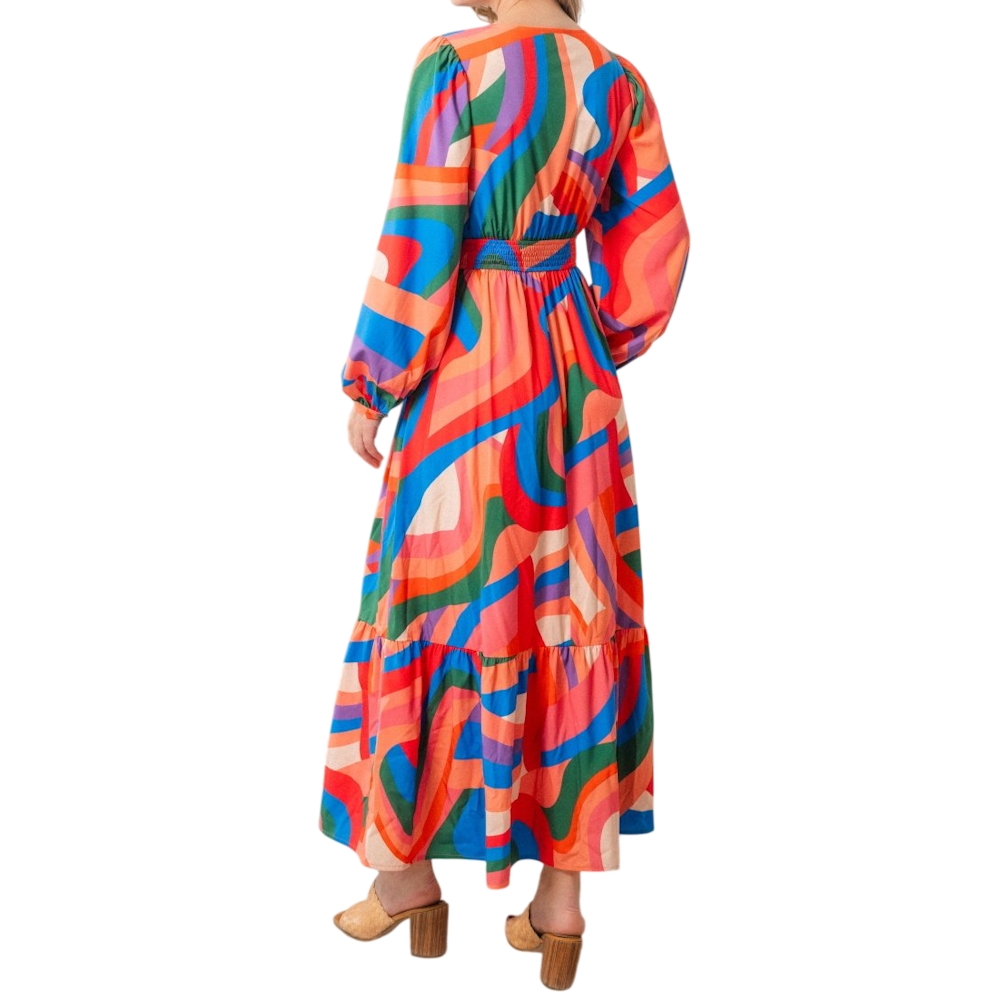 Back view of a woman wearing a long-sleeved maxi dress with a colorful, vibrant abstract swirl pattern.