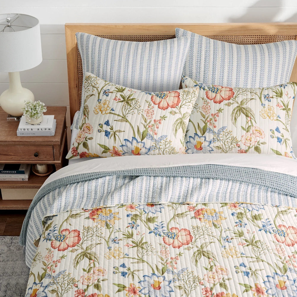 Multicolor floral quilt set with matching pillow shams and blue striped accents on a bed.