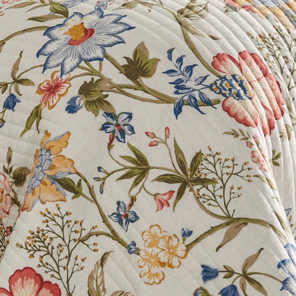 Close-up of a white quilt with a colorful floral botanical pattern of blue, red, and yellow flowers.