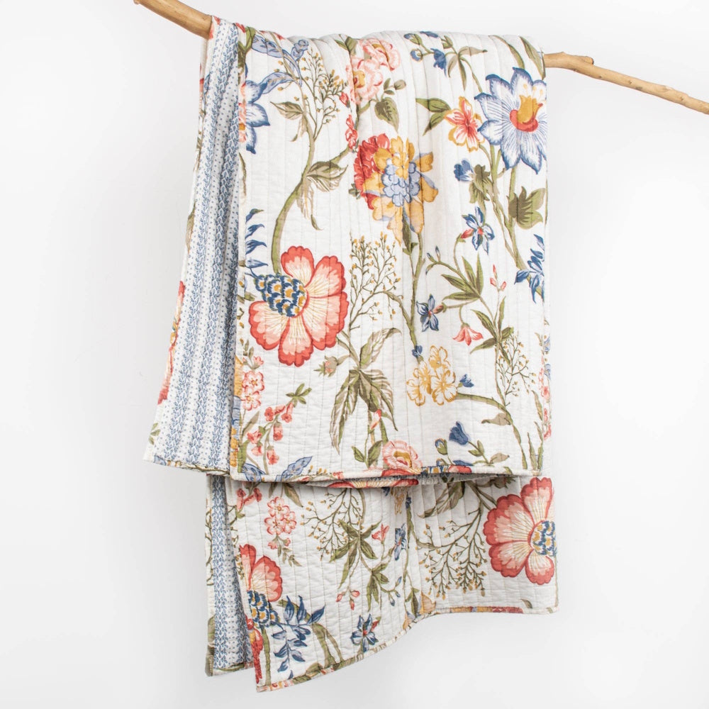 A hanging quilted blanket with a vintage-style blue, red, and yellow floral pattern on a white background.