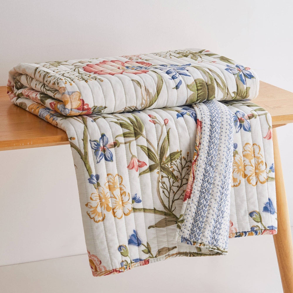 Multicolor floral Maileen quilted throw blanket with vertical stitching on a wooden table.