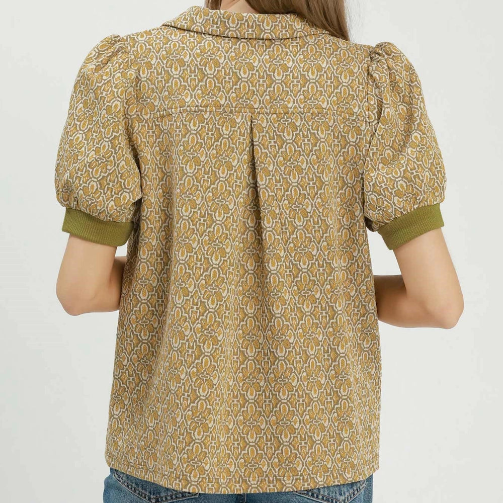 Back view of a mustard yellow printed top with short puff sleeves, a collar, and green ribbed cuffs.