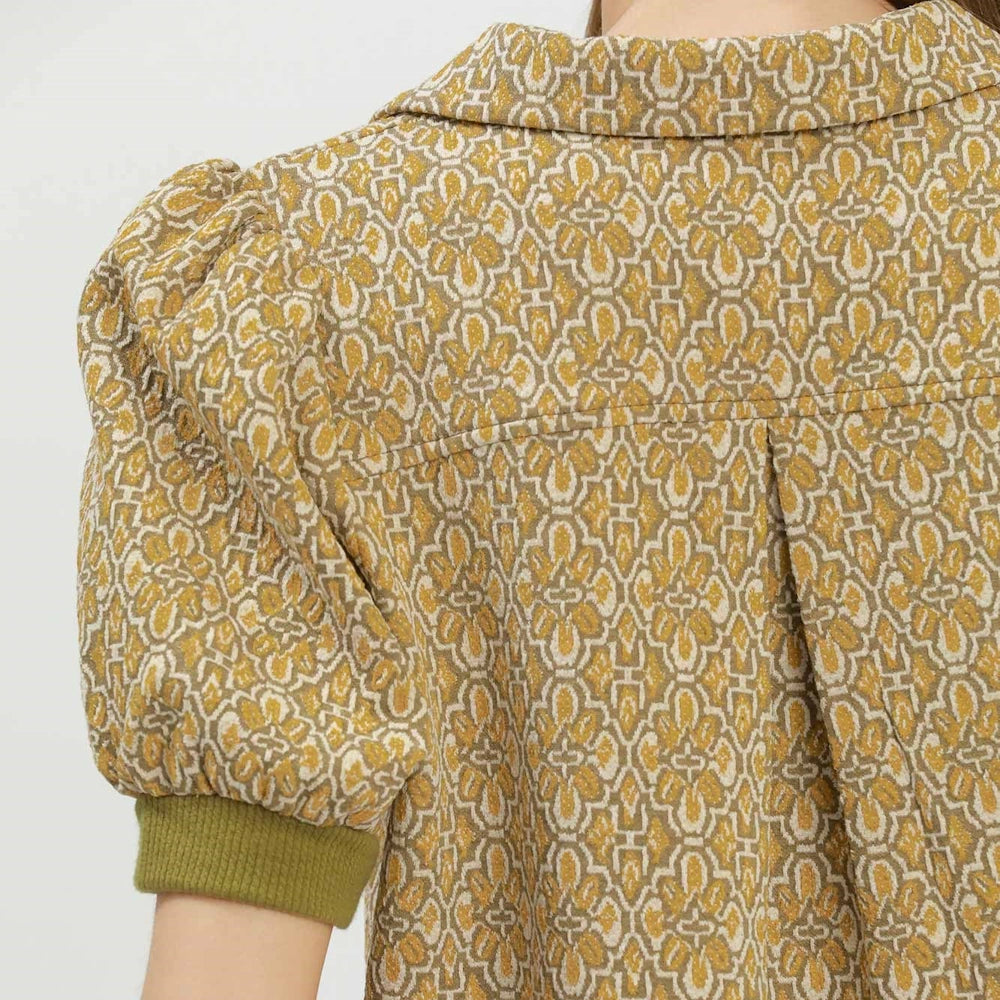 Close-up back view of a mustard yellow patterned collared top with short puff sleeves and olive ribbed cuffs.