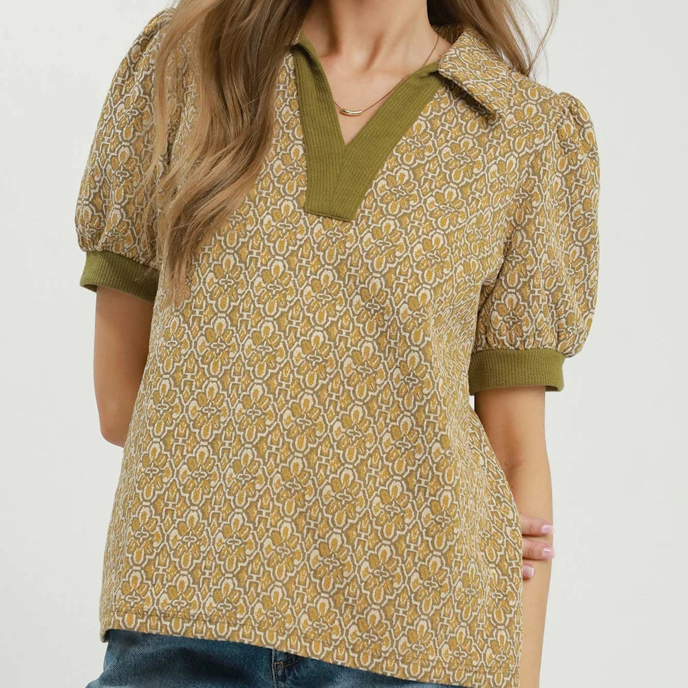 Woman wearing a mustard printed collared top with olive trim and puff sleeves.