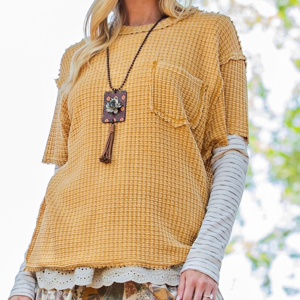Woman wearing a mustard yellow waffle-knit top layered over a striped long-sleeve shirt and a long necklace.