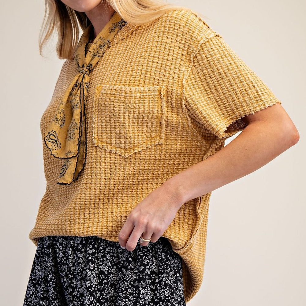 A person wearing a mustard yellow waffle-knit short-sleeve shirt with a matching neck scarf.
