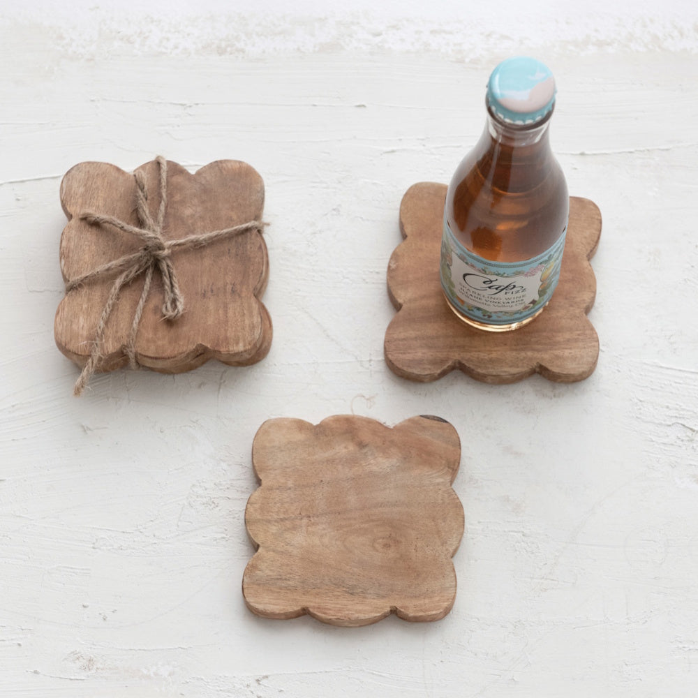 Natural mango wood scalloped coasters set with a beverage bottle on a white textured background.