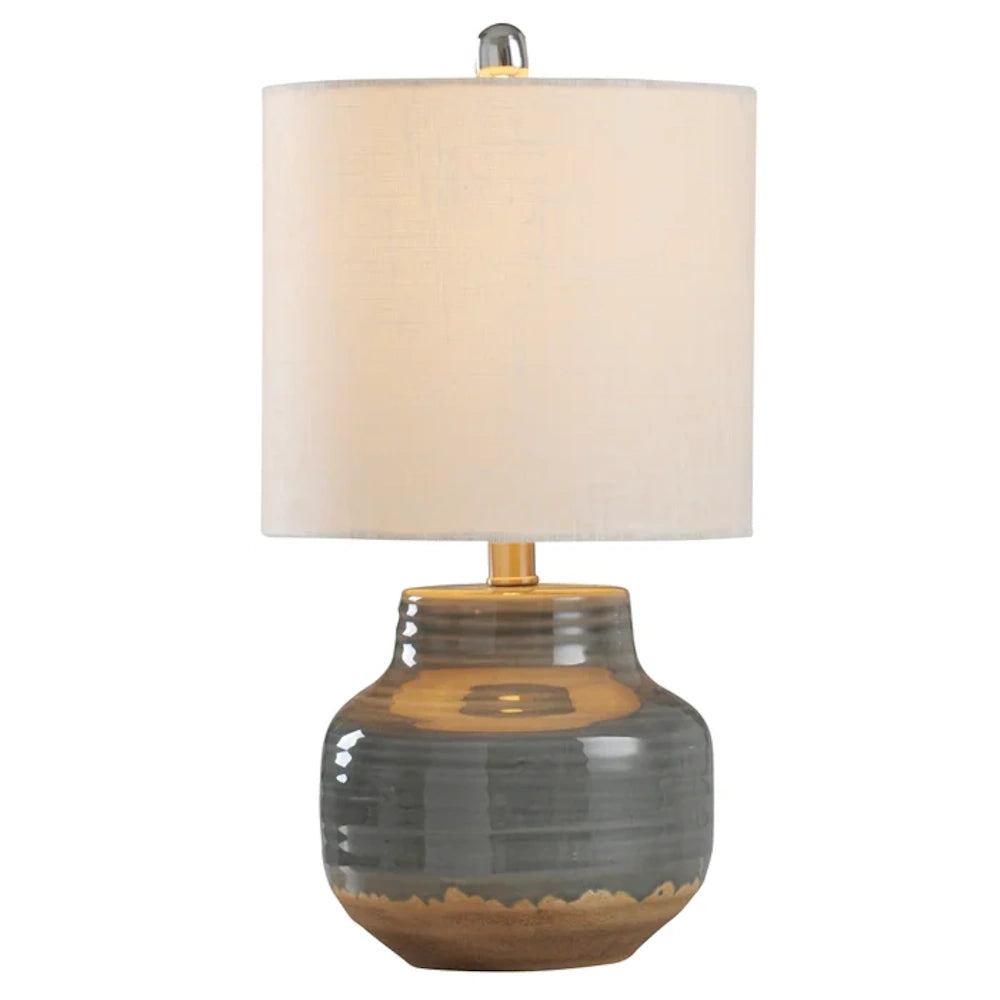 Rustic gray ceramic table lamp with a ribbed, jar-shaped base, gold accents, and a neutral fabric drum shade.