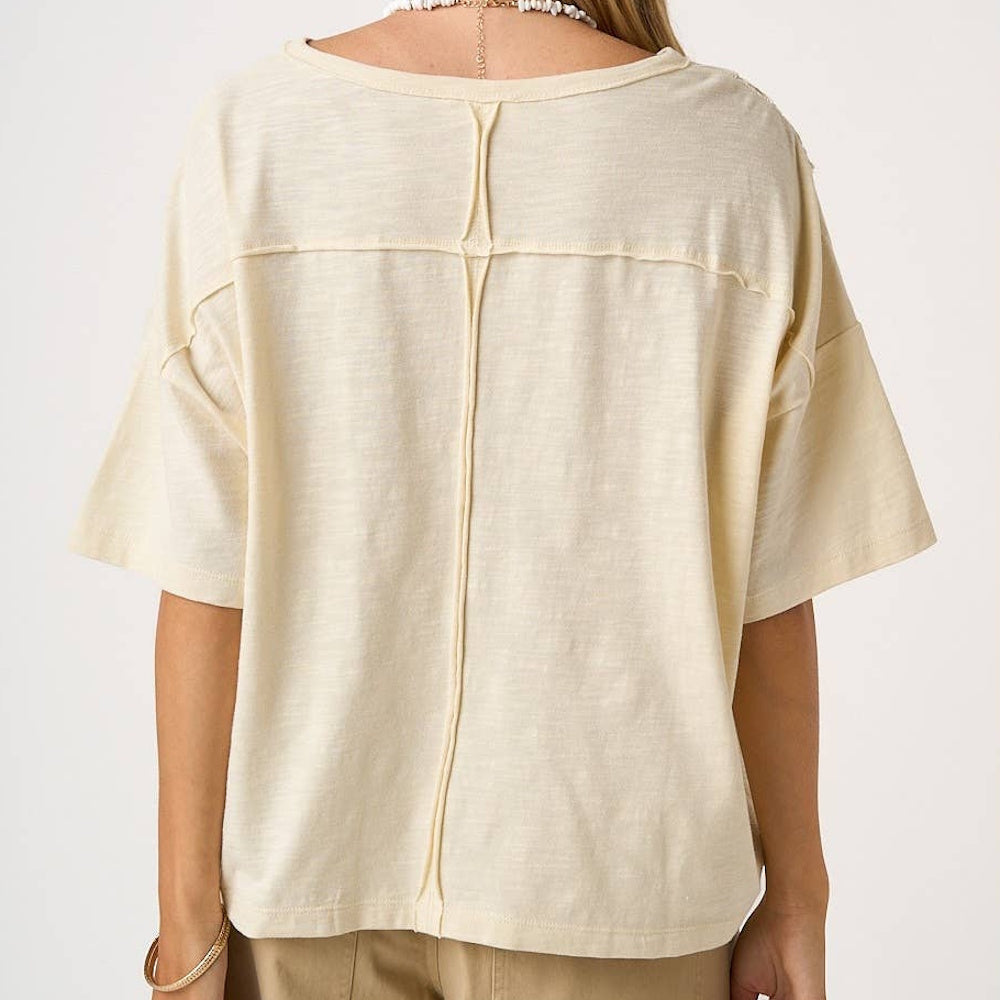 Back view of a cream-colored patchwork short sleeve top with exposed seam detailing and a relaxed fit.