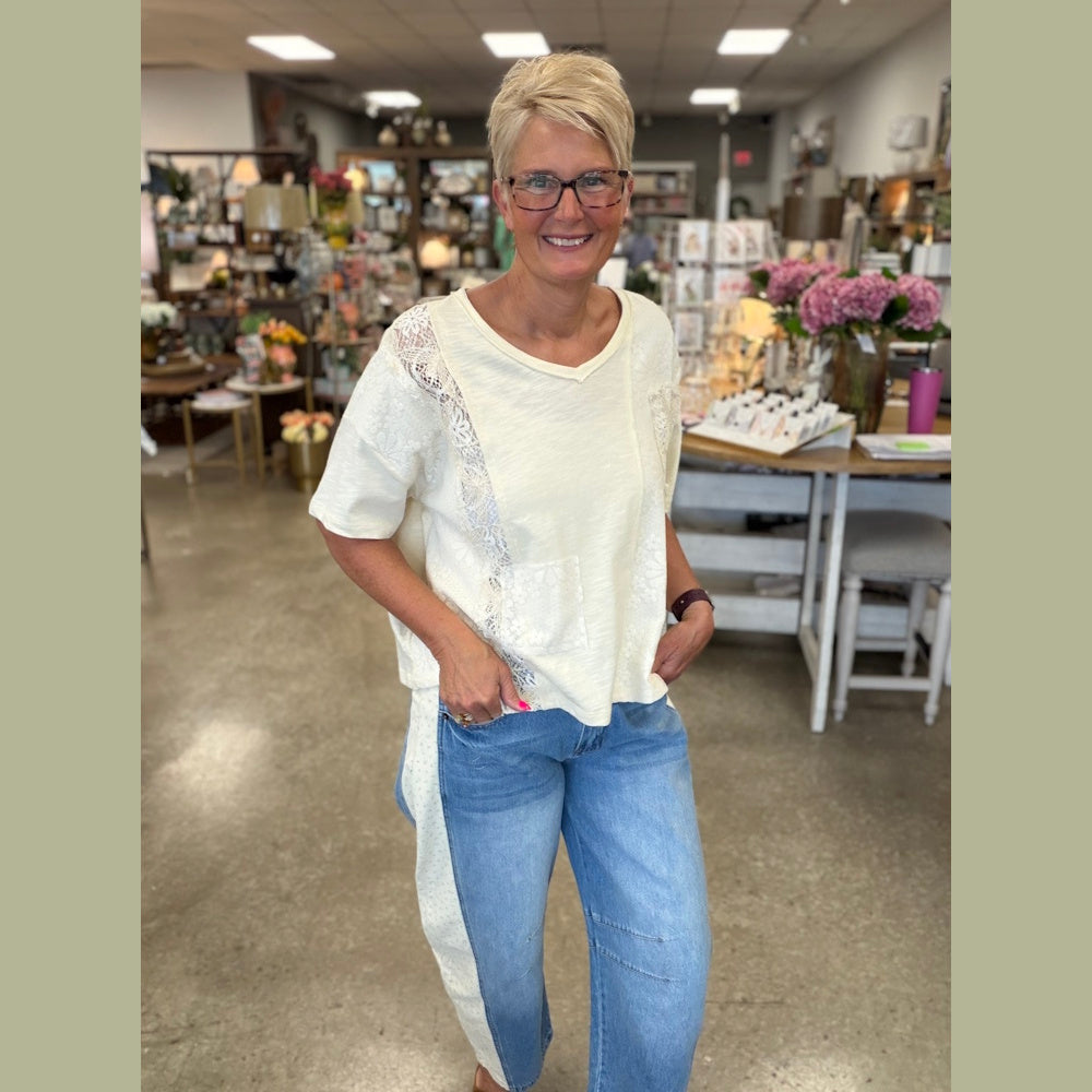 A woman in a cream lace-patchwork top and side-stripe jeans smiling in a boutique.