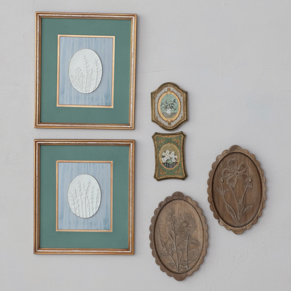 Vintage gallery wall with framed botanical art, small ornate frames, and carved scalloped wood flower plaques.