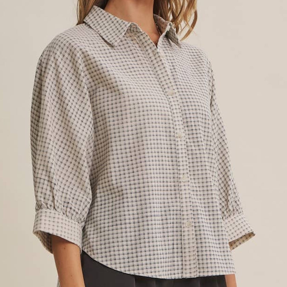 Side view of a woman wearing a light-colored micro-grid plaid button-down shirt with three-quarter sleeves.