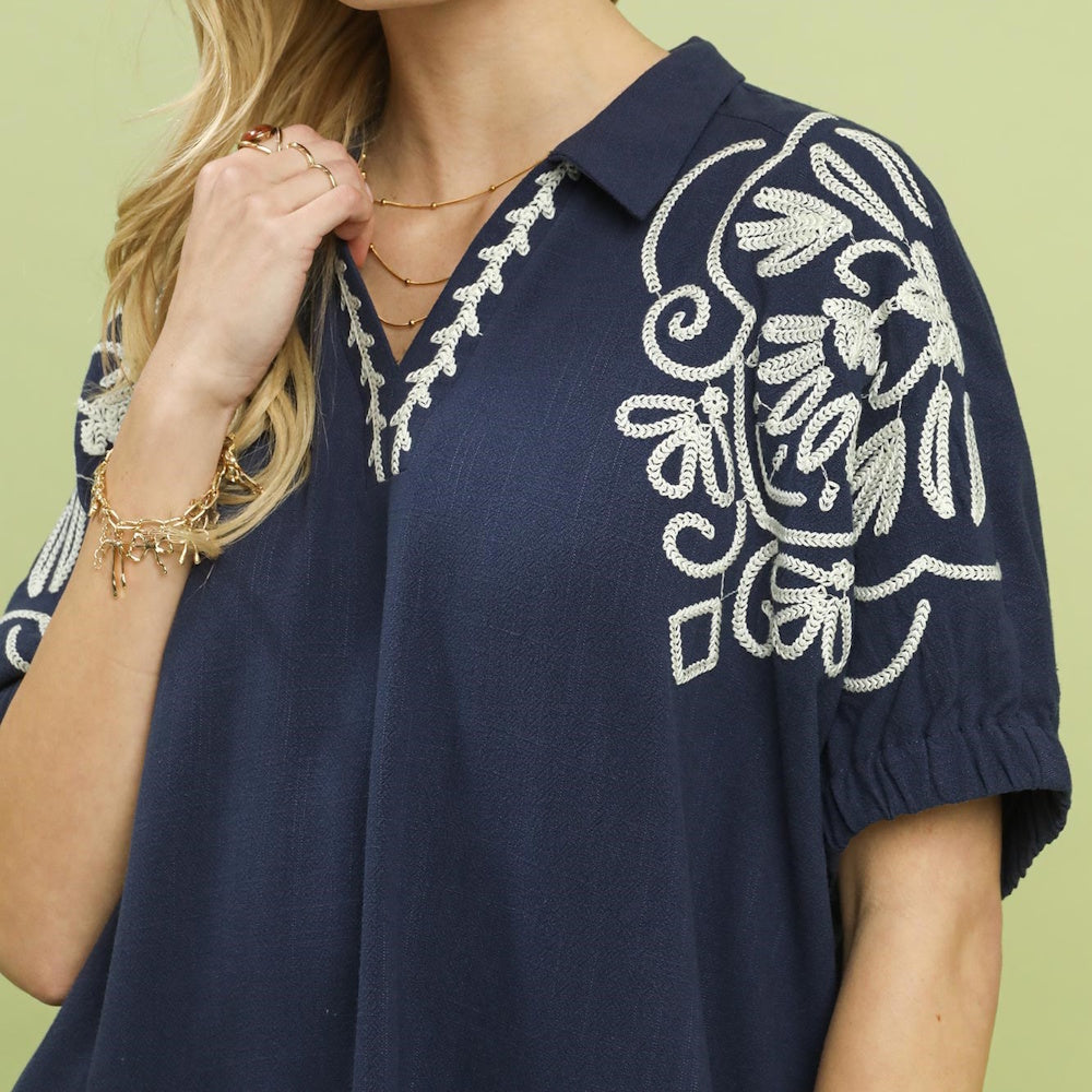 Close-up of a navy embroidered v-neck dolman top with an open point collar.