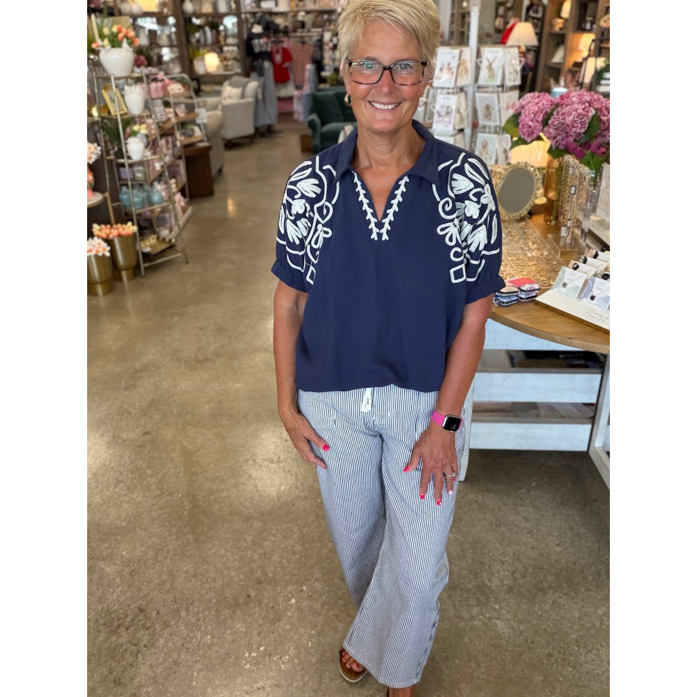 Woman in navy embroidered v-neck dolman top and striped pants.