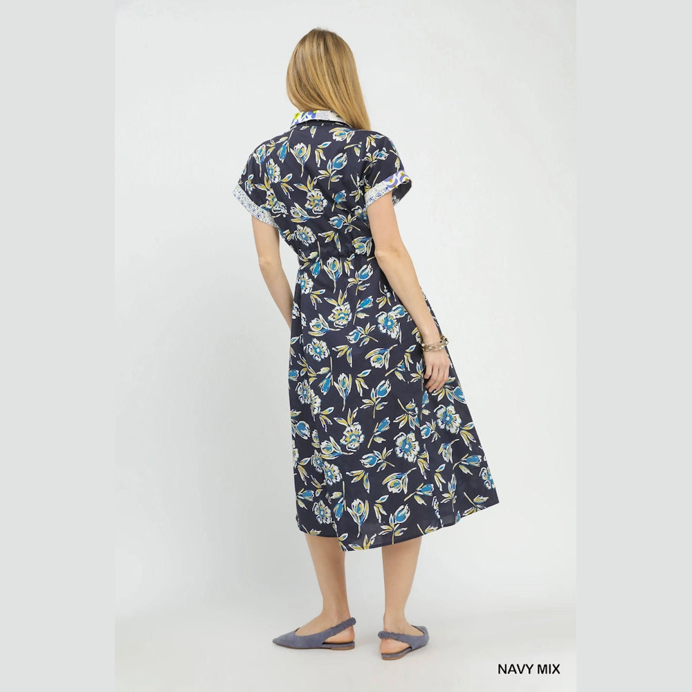 Back view of a woman wearing a navy mix floral button-front midi dress with short sleeves and a cinched waist.
