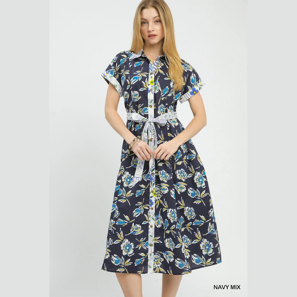 Woman in a navy blue floral button-front midi dress with a tie belt and cuffed short sleeves against a white background.