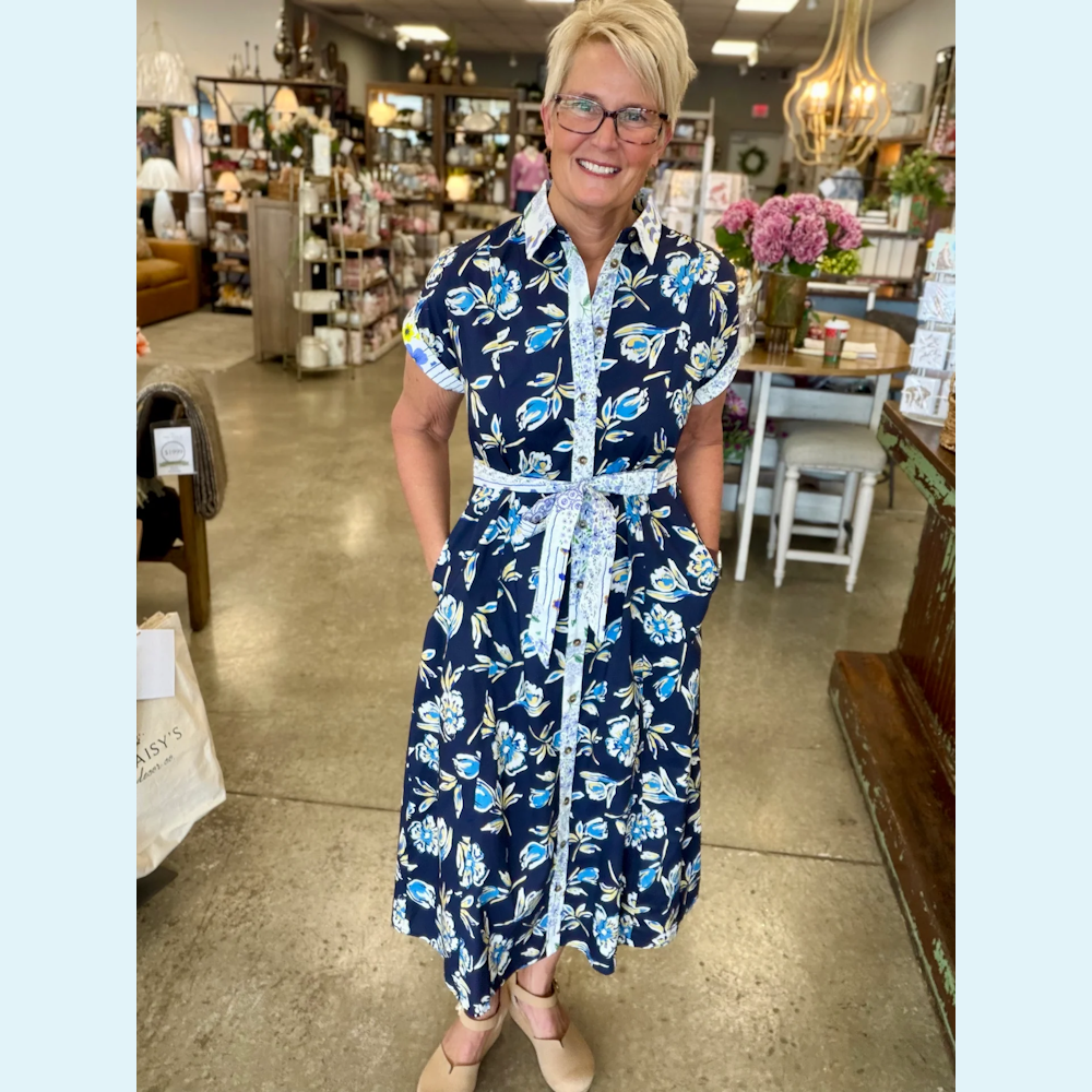 Woman in a navy blue floral midi shirt dress with a tie belt, button front, and cuffed short sleeves in a shop.