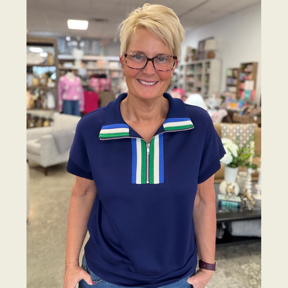 Woman in navy short-sleeve half-zip knit top with green, white, and blue striped collar detailing and glasses.