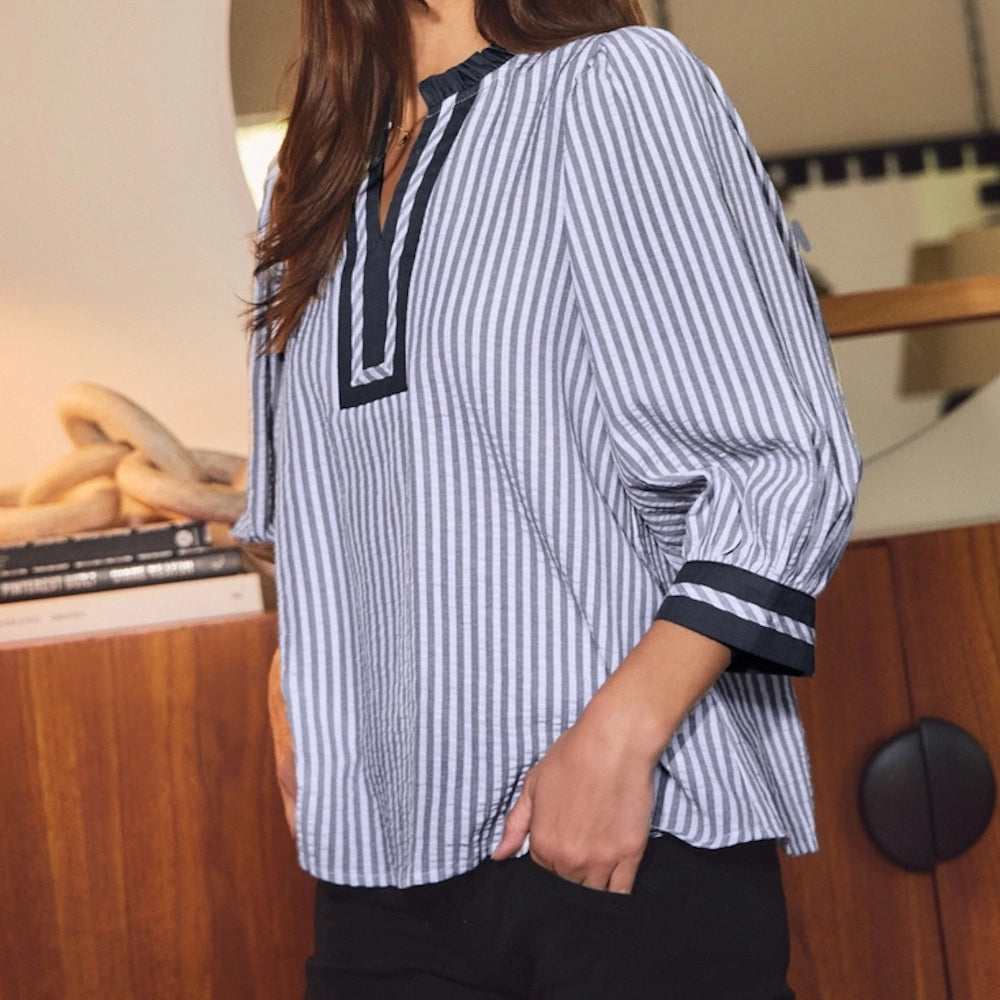 Woman wearing a navy blue and white vertical striped woven blouse with a split neckline and 3/4 sleeves.