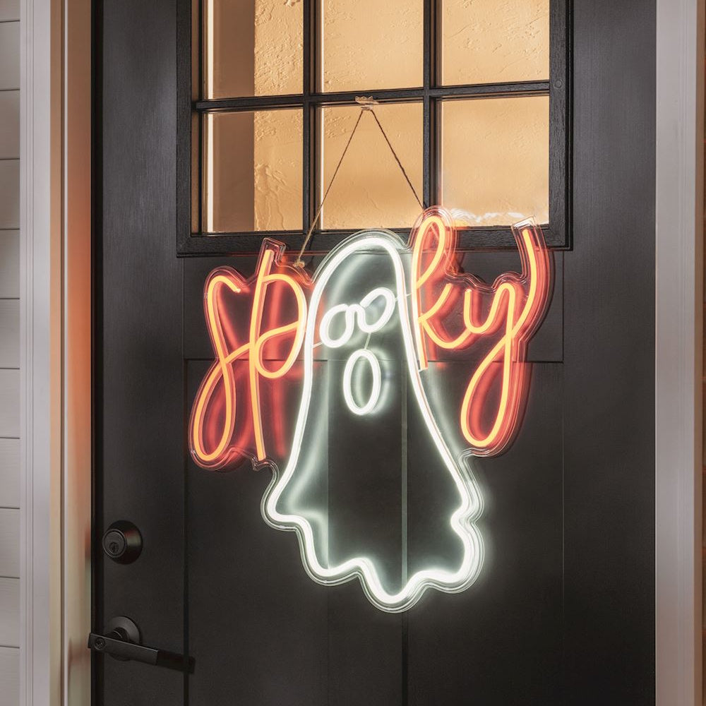 A glowing neon Halloween ghost sign that says "Spooky" hanging on a dark front door with glass panels.