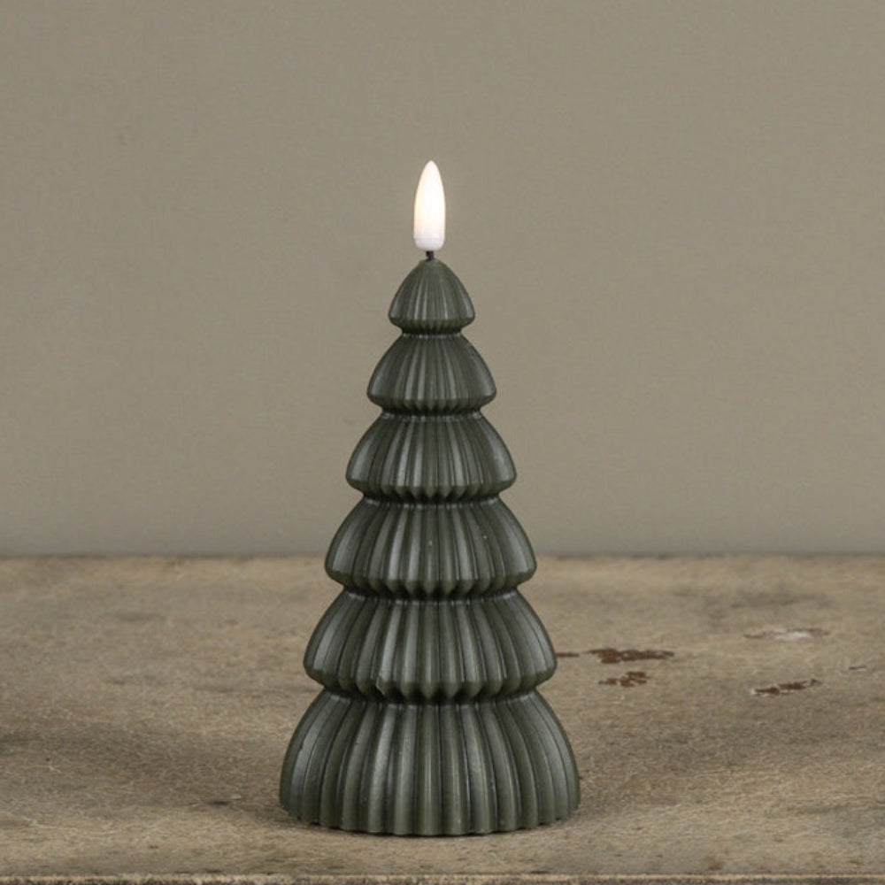 Dark green Christmas tree-shaped flameless candle with a glowing flame tip on a stone surface.