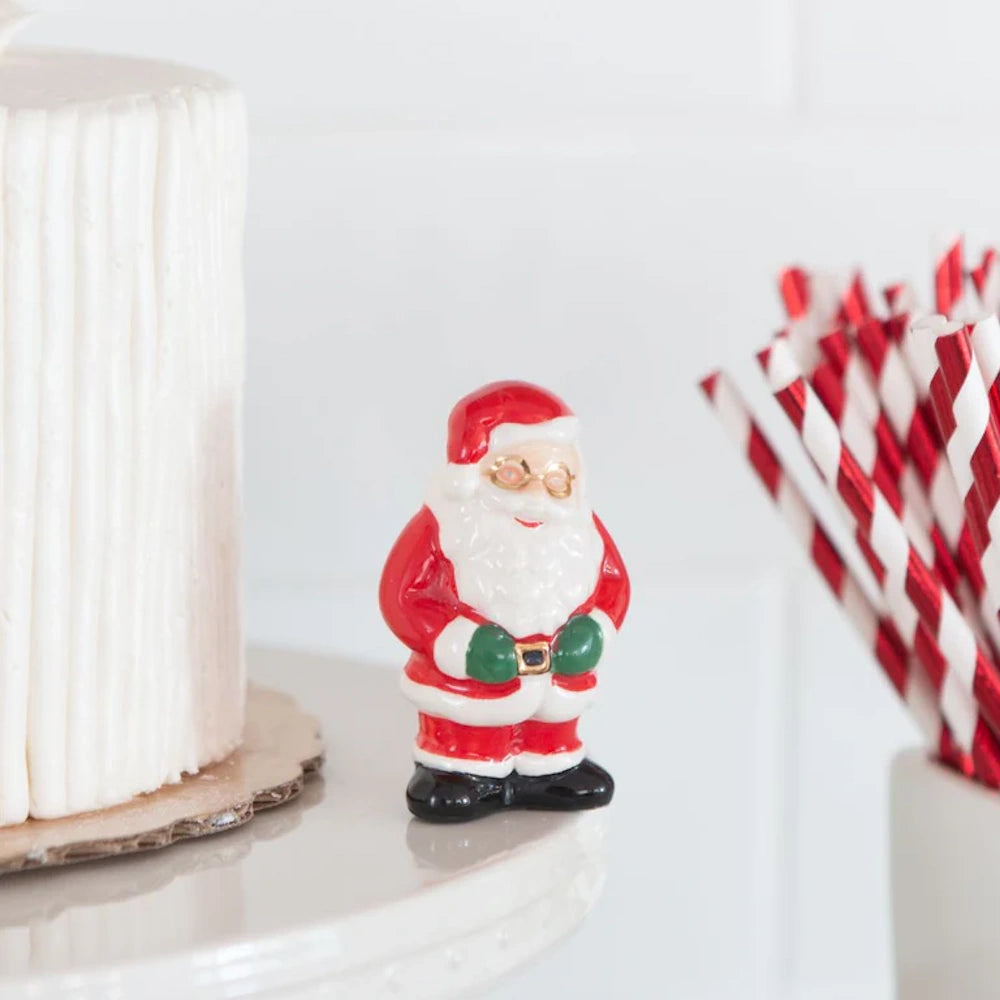A ceramic Santa Claus figurine with green mittens and glasses, standing on the edge of a cake stand.