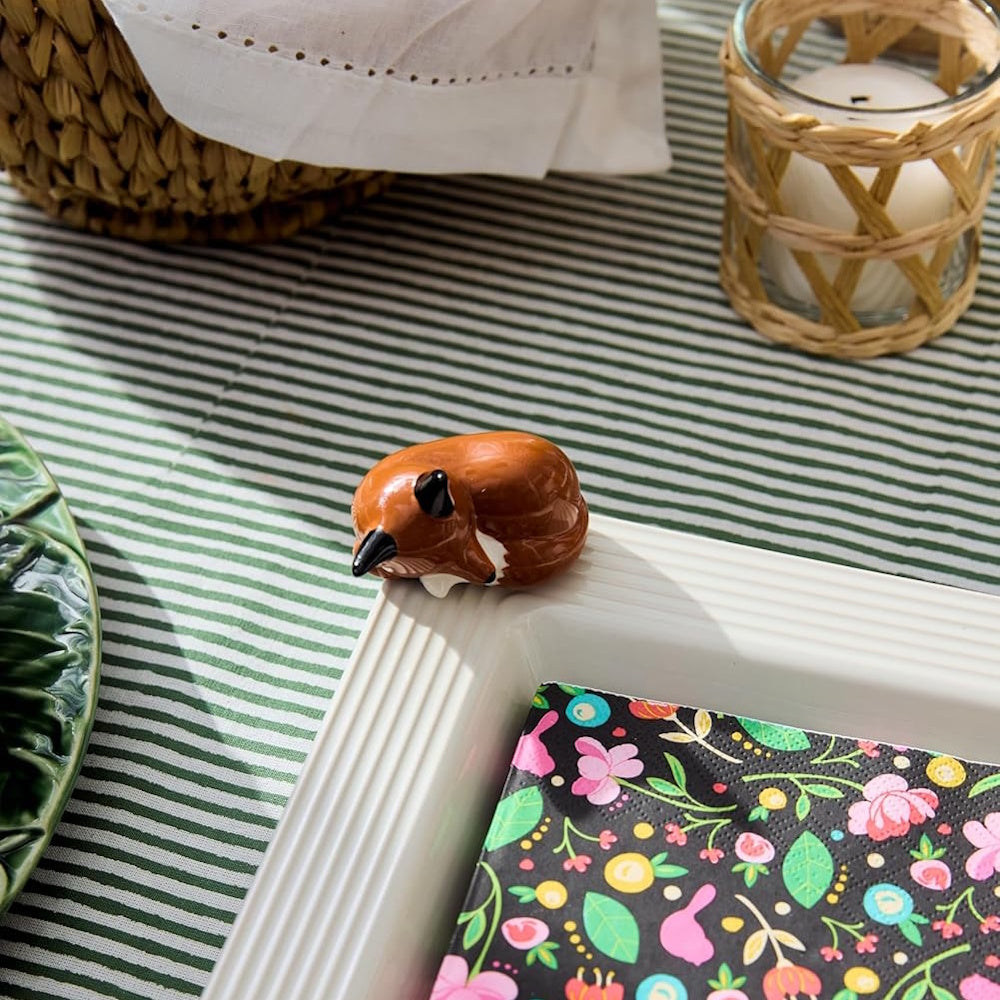 A small ceramic sleeping fox figurine attached to the rim of a white serving platter.