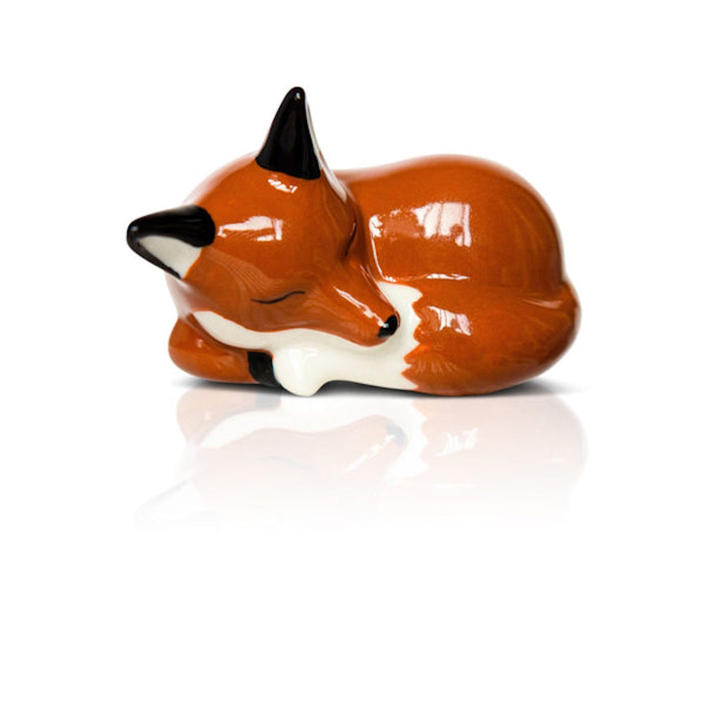 Glossy ceramic figurine of a sleeping orange fox curled up on a reflective white surface.
