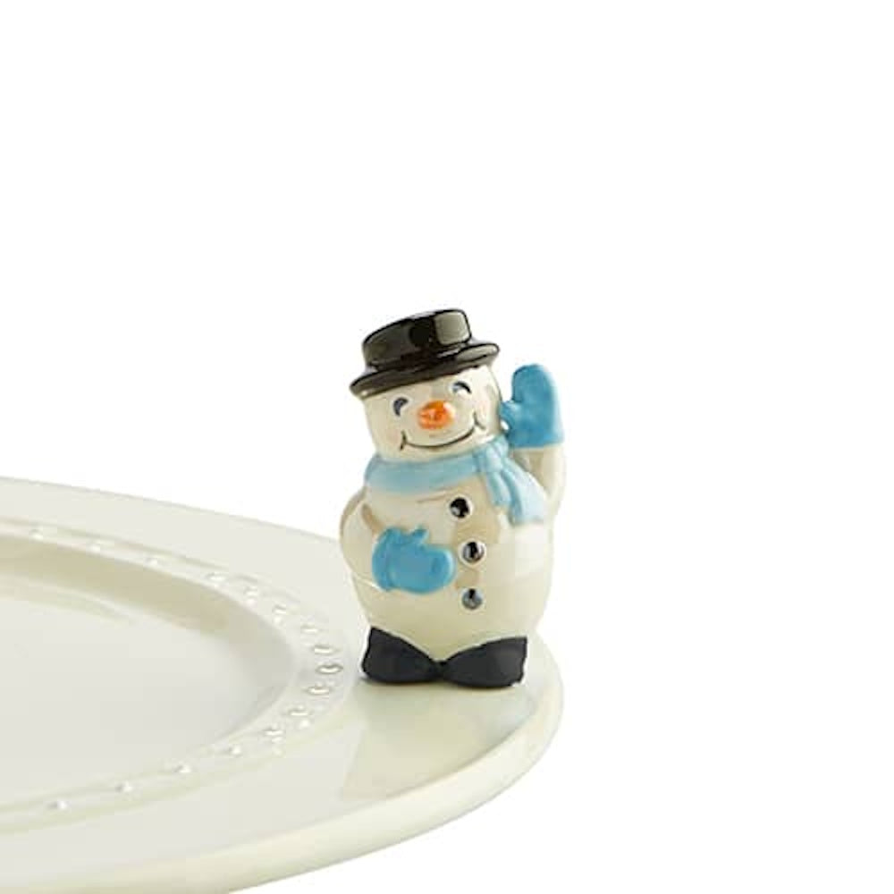 A smiling ceramic snowman figurine wearing a black top hat and blue scarf, waving from the edge of a plate.