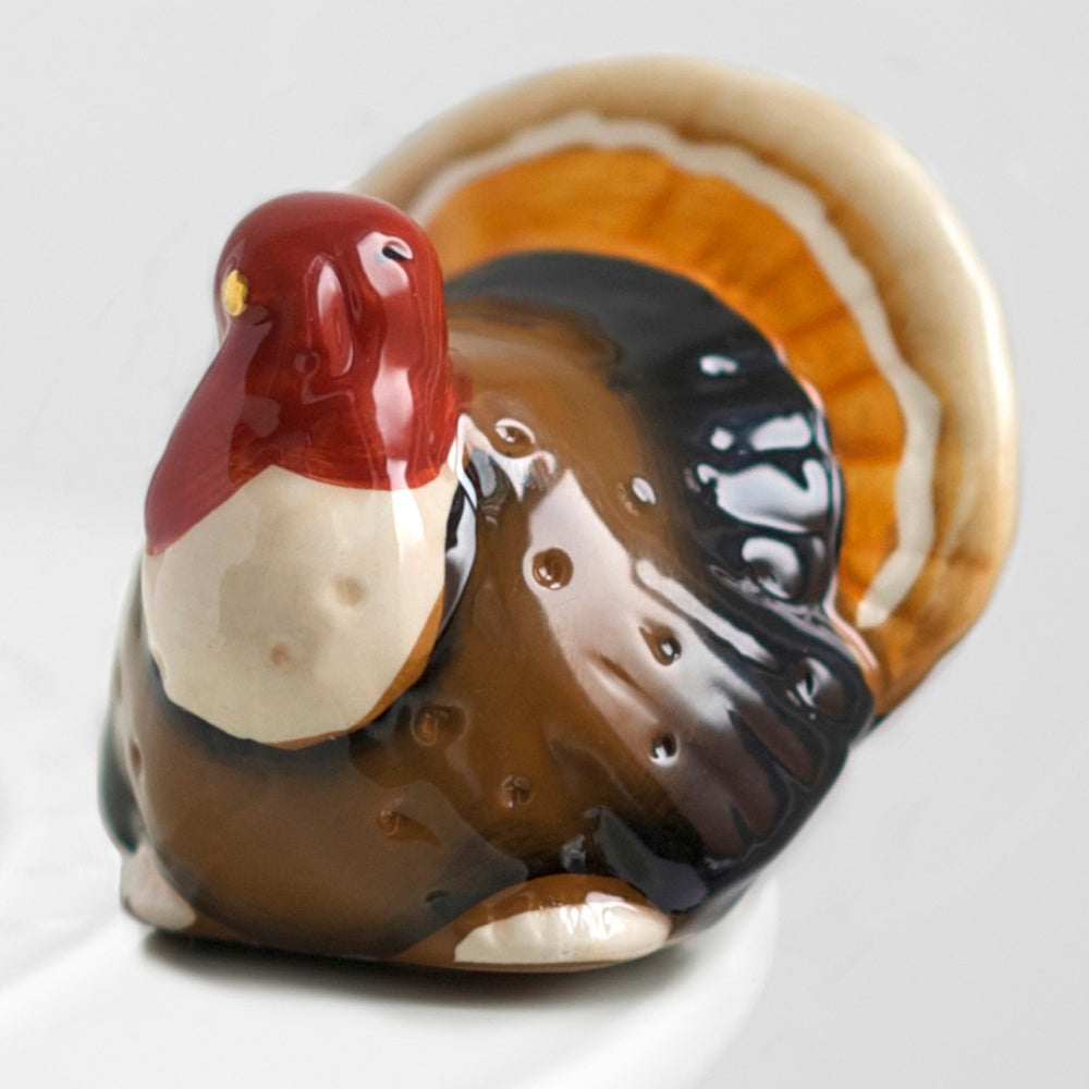 Small ceramic turkey figurine with a glossy finish, featuring a red head, brown body, and fanned tail.