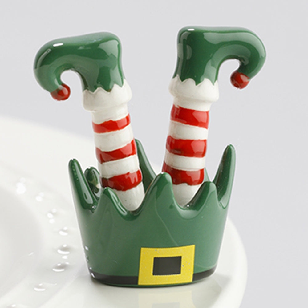 A small ceramic Christmas elf figurine featuring upside-down striped legs sticking out of a green elf hat.