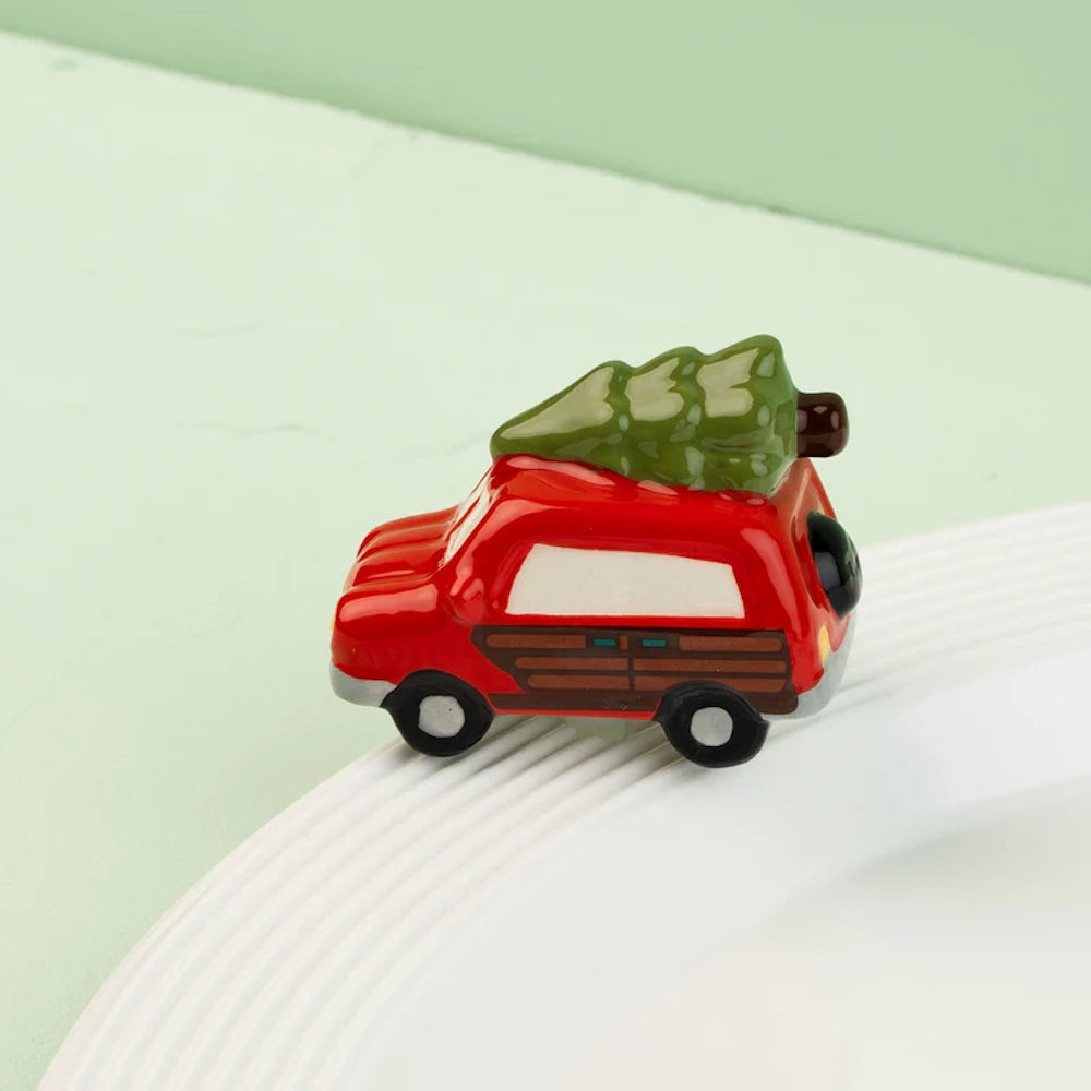 A small ceramic red station wagon figurine with a green Christmas tree strapped to the roof.