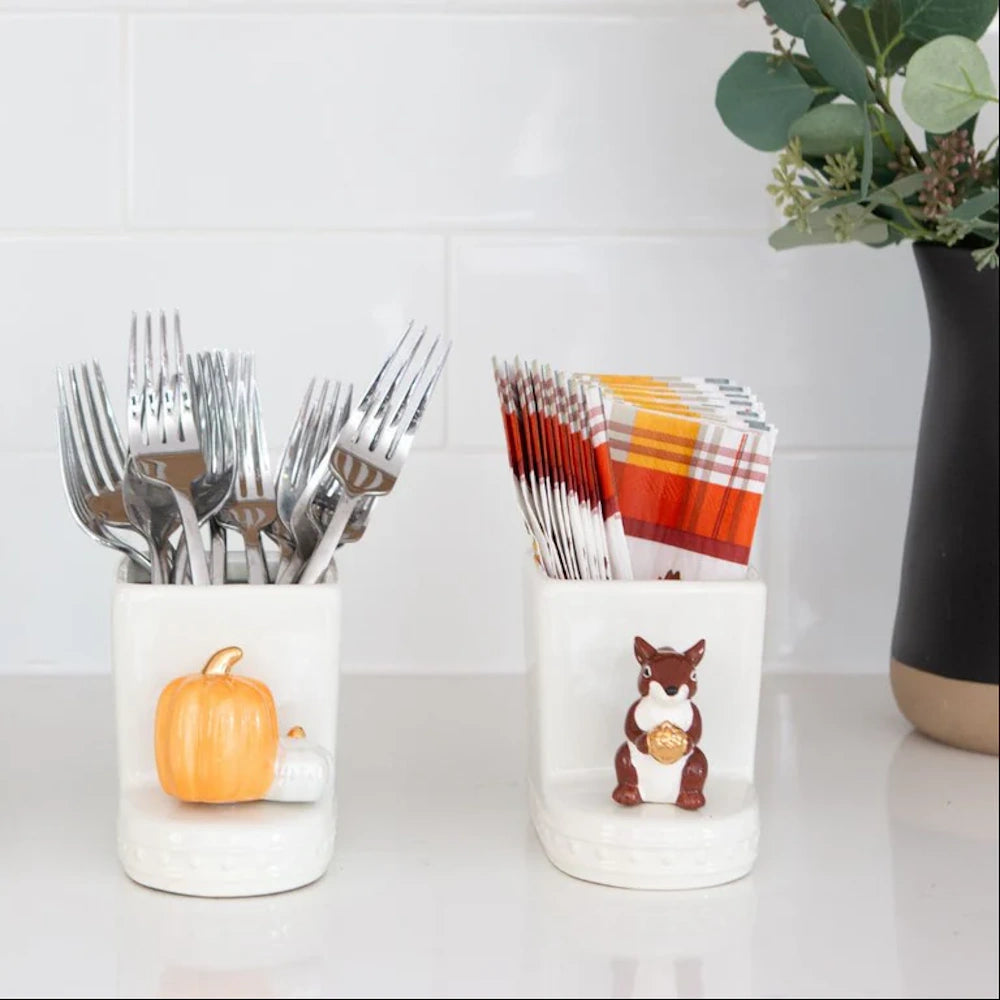 Two white ceramic holders: one with forks and a pumpkin charm, the other with autumn napkins and a squirrel.