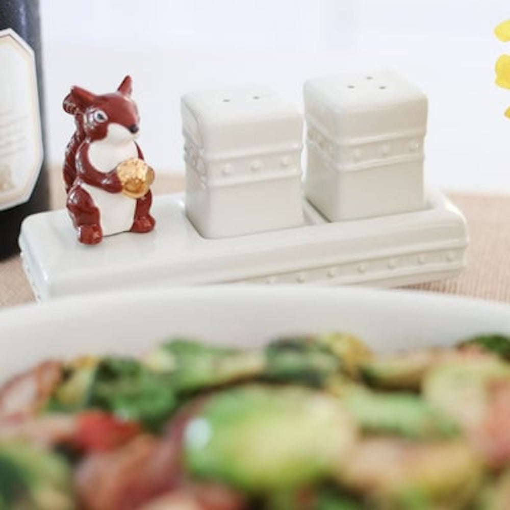 White ceramic salt and pepper shakers on a tray with a small brown squirrel holding a gold acorn.