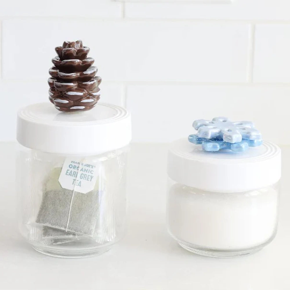 Two glass jars with white lids: one holds Earl Grey tea with a pinecone topper; the other holds sugar.