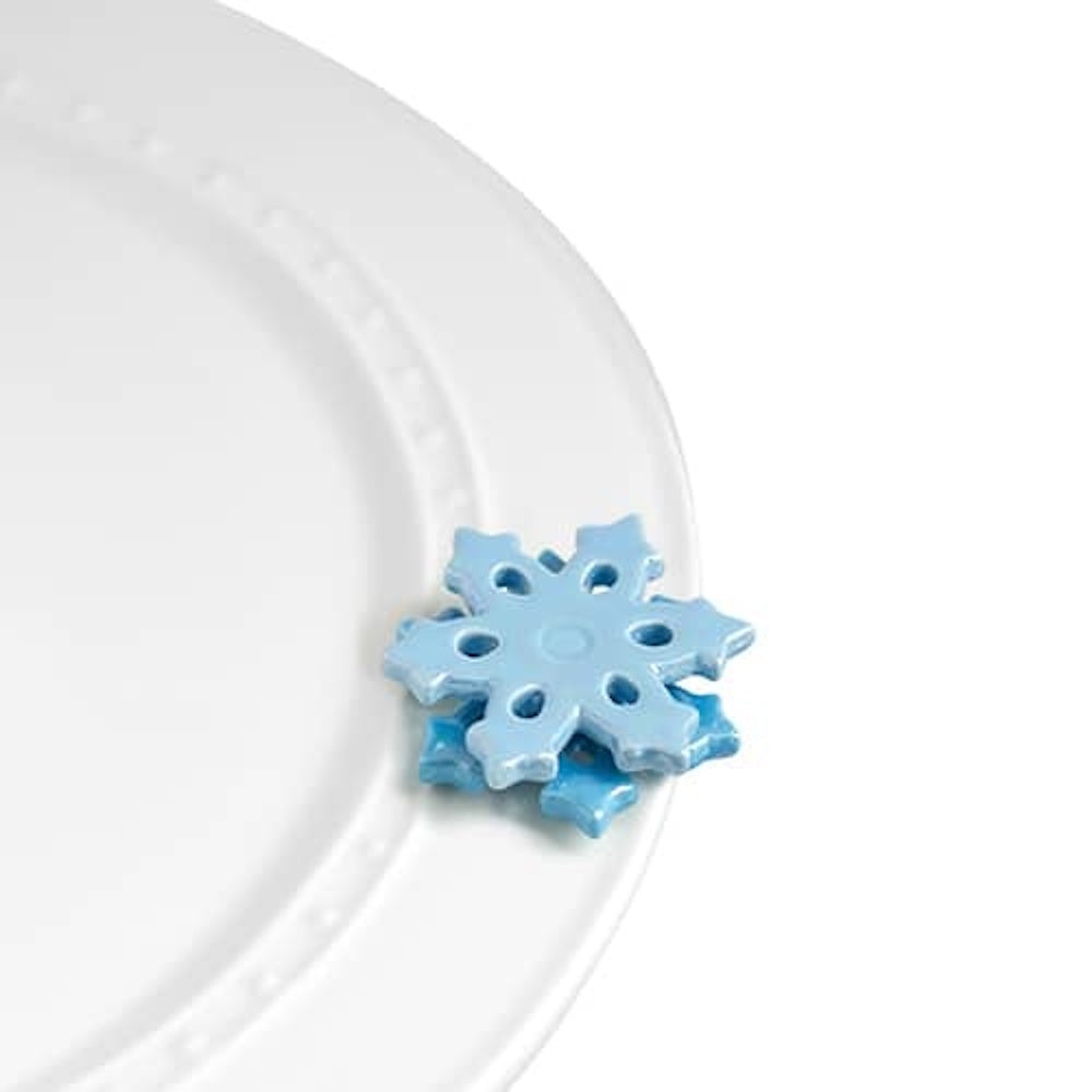A glossy, light blue ceramic snowflake charm rests on the rim of a white serving platter.