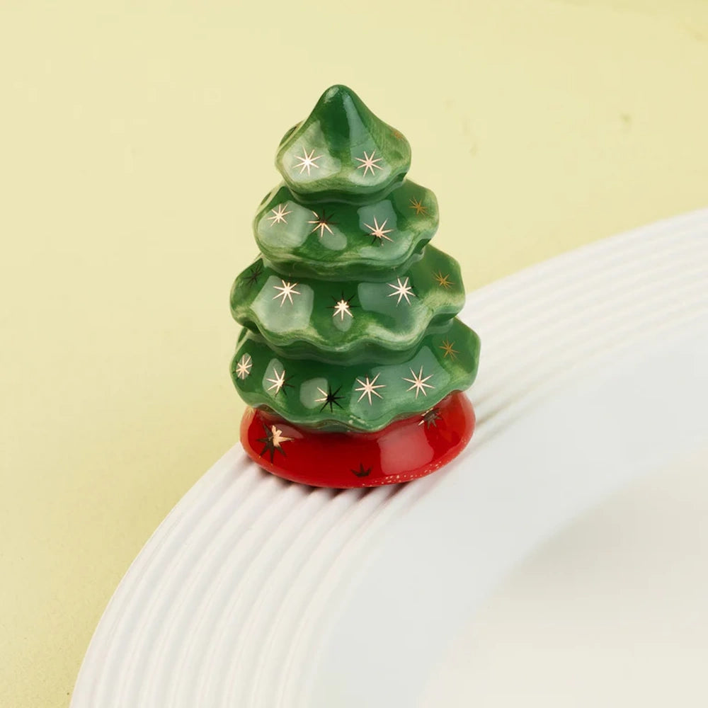Ceramic Christmas tree figurine with gold stars and a red base, attached to the rim of a white ceramic plate.
