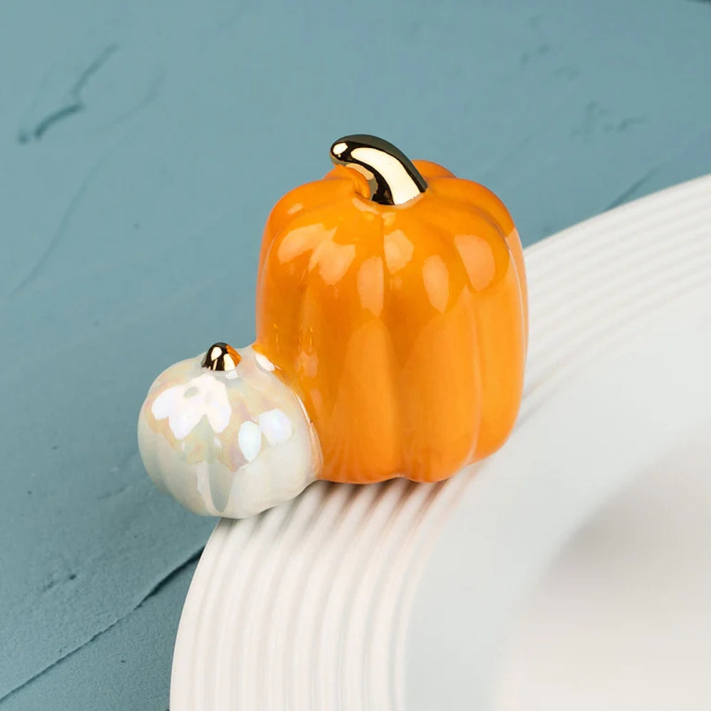 Ceramic orange and iridescent white pumpkins with gold stems, resting on the rim of a white plate.