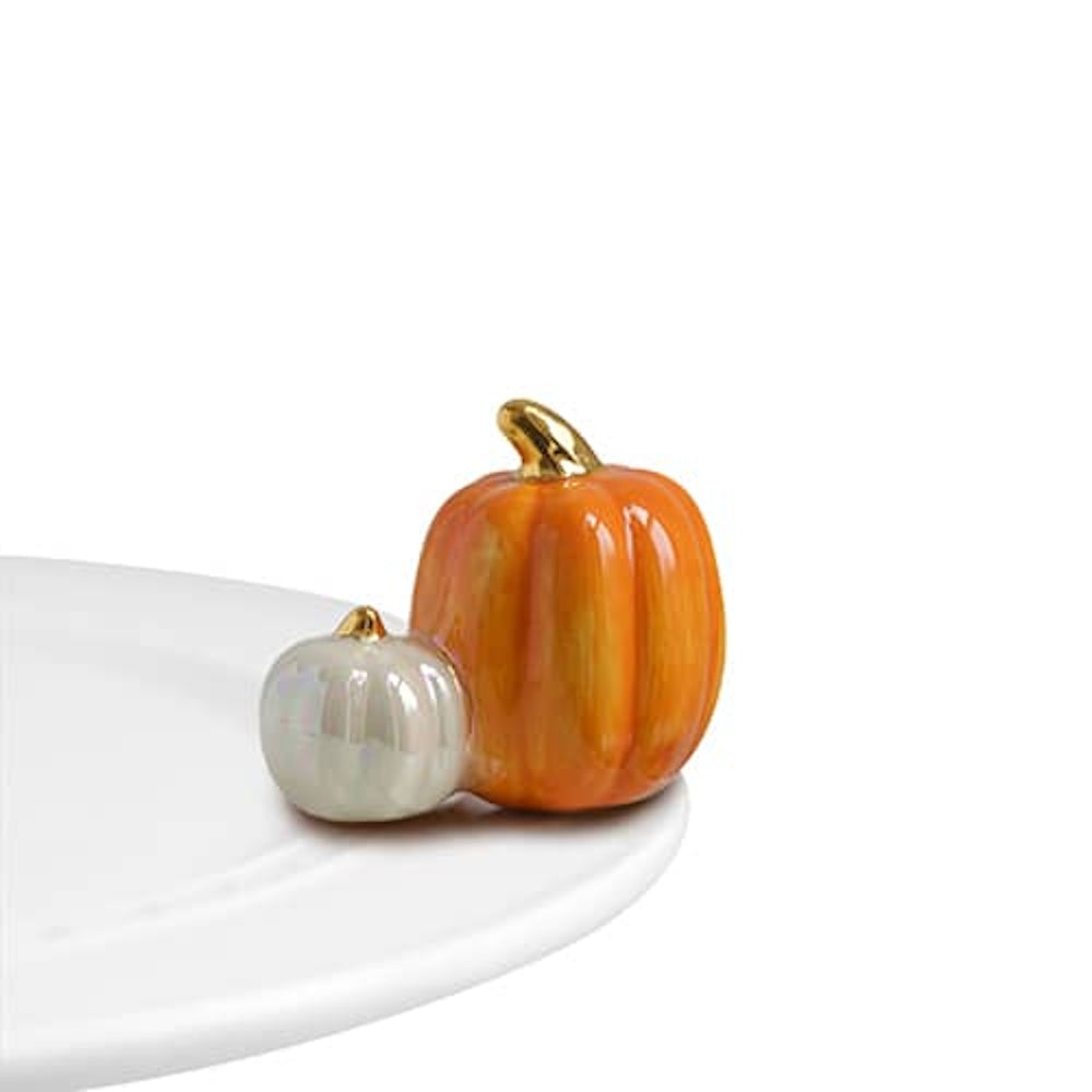 Ceramic orange and iridescent white pumpkins with gold stems sitting on the rim of a white platter.