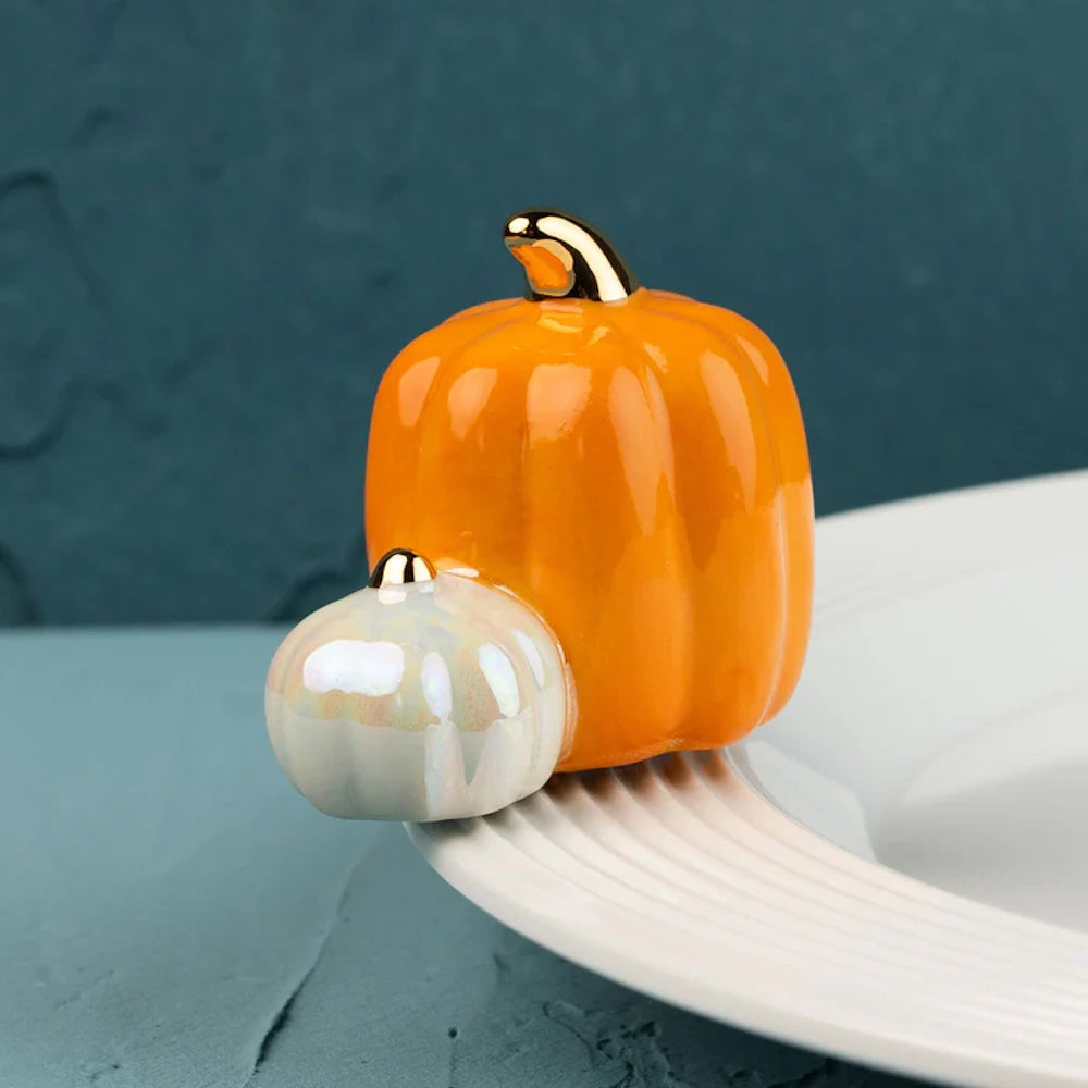 Ceramic orange pumpkin and small white gourd figurine with gold stems, resting on the rim of a white plate.