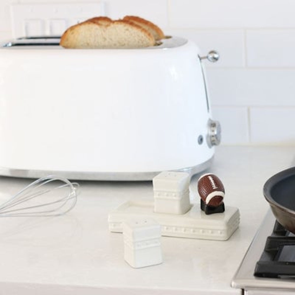 A ceramic football figurine attached to a white salt and pepper shaker holder next to a white toaster.