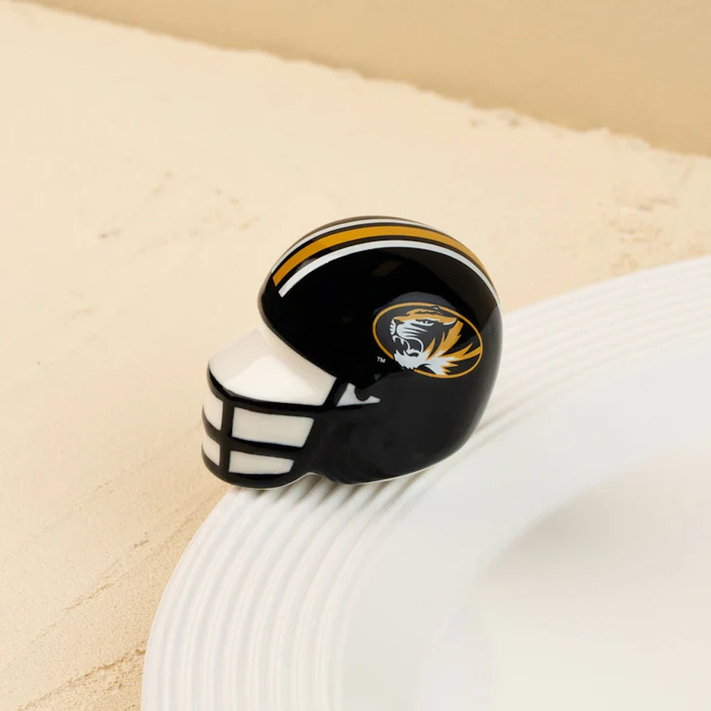 Small ceramic black football helmet figurine with a tiger logo and gold stripes on a white plate rim.